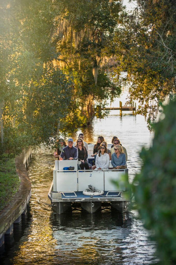 A tour pontoon with passengers moving down a narrow canal lined with moss-draped trees